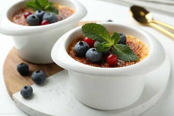 Delicious creme brulee with berries and mint in bowls on white table, closeup