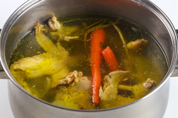 Chicken broth with pieces and vegetables in a metal pot.