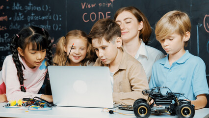 Closeup of boy using laptop programing engineering code and writing program while group of diverse...