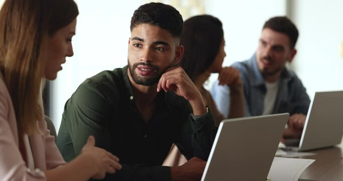 Multiethnic teammates working on joint task, planning strategy, search solution engaged in teamwork, brainstorming, learn new program using laptop, sit at desk in co-working. Business, communication
