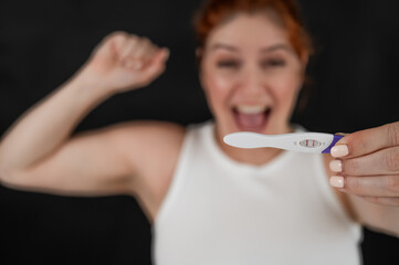 Blurred portrait of happy caucasian woman holding positive express pregnancy test on black...