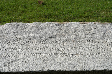 Inscriptions of Tamil language carved on the stone with green grass in the background. Indian rock...