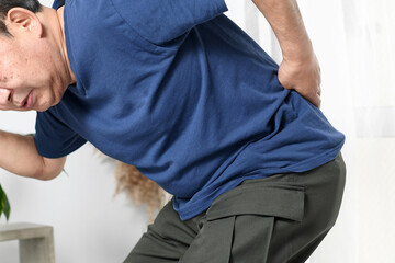 腰痛のため腰を押さえるアジア系の高齢男性
