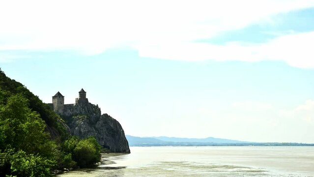 Time lapse of medieval castle on top of hill and river flowing under blue sky