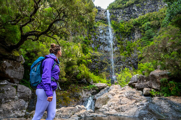Naklejka premium Low angle shot of female tourist with backpack enjoing the natural atmosphere at high waterfall. Lagoa do Vento waterfall, Madeira Island, Portugal, Europe.