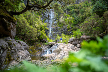 Female tourist with backpack walks up rocks to a picturesque waterfall. Lagoa do Vento waterfall,...