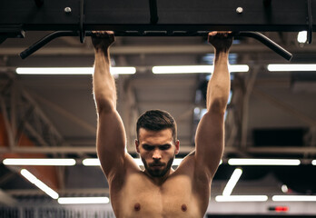front view of a strong man doing pull ups in a gym
