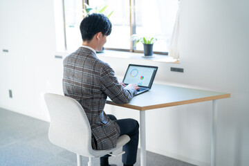 オフィスでパソコン作業をするジャケットを着た若い男性