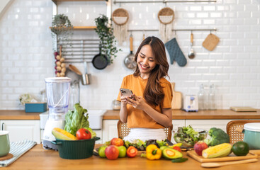Portrait happy beauty slim healthy asian woman use phone and vegan food healthy fresh vegetable and fruit in kitchen.diet, vegetarian, eating, fruit, wellness, health, green food.Fitness, healthy food - obrazy, fototapety, plakaty