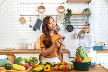 Portrait happy beauty slim healthy asian woman use phone and vegan food healthy fresh vegetable and fruit in kitchen.diet, vegetarian, eating, fruit, wellness, health, green food.Fitness, healthy food
