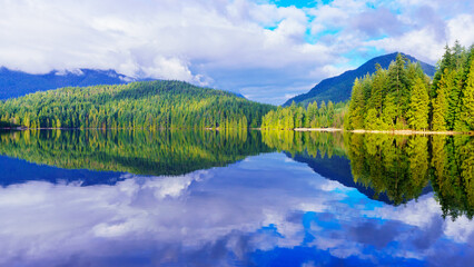 Clouds reflected in lake with forest and mountain background.