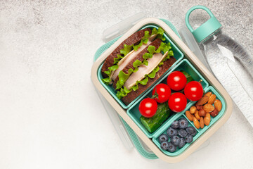 School lunch box. Ham and cheese sandwich, vegetables, nuts and berries in a plastic container. Top view. Back to school concept. Copy space