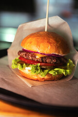 Burger with cheese on wax paper on plastic tray on wooden table. Fresh tasty burger on dark background. Close up. High quality photo
