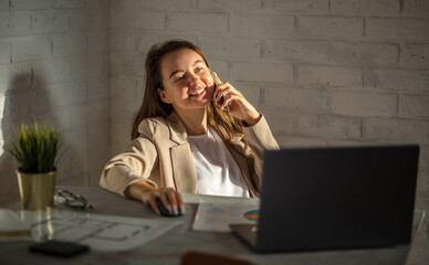 Smiling businesswoman using her phone in the office. Small business entrepreneur talking on mobile phone and smiling while communicating in office