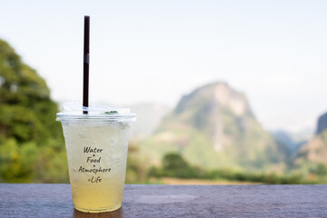 Work life balance and chilling relax travel with honey lemon soda cold beverage for drink in plastic cup take away on a wood table with nature mountain landscape in forest
