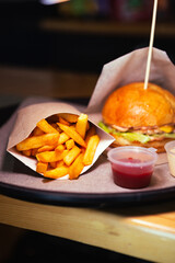 Side view of fresh cheeseburger with chicken and fries with red sauce on wooden table. High quality photo. Selective focus. Unhealthy eating concept
