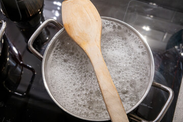Hot pasta water boiling on a stove with a wooden spoon to prevent boil over.