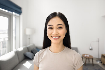 Cheerful happy Asian girl home head shot portrait. Young Chinese woman standing in living room,...