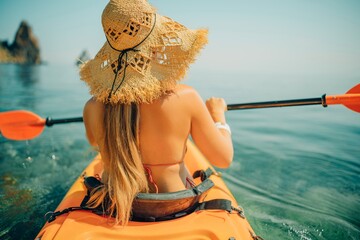 Woman in kayak back view. Happy woman with long hair in a swimsuit and hat floating in kayak on the...