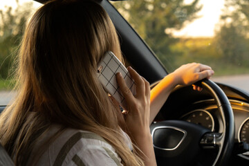 Young woman using mobile phone while driving car on highway road during sunset. Womandriver has accident calling with smartphone for help. Business woman busy driving