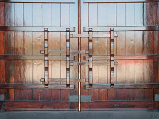 Front view of the entrance door handle of a Chinese temple. It is a large wooden door, grooved, dark red color, traditional wood lock structure.