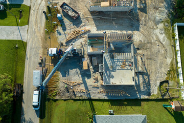 Aerial view of lifting crane and builders working on unfinished residential house with wooden roof frame structure under construction in Florida suburban area