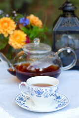 Obraz na płótnie Canvas Patio table with cup of tea, pot, flowers and lantern.