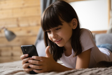 Child and cellphone. Smart little hispanic girl relax lie on bed look on cell screen watch video...