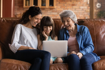 Funny cartoon. Happy intergenerational hispanic family of older grandmother adult mommy and preteen girl daughter grandchild spend free time on couch laugh enjoy cute video movie on laptop computer