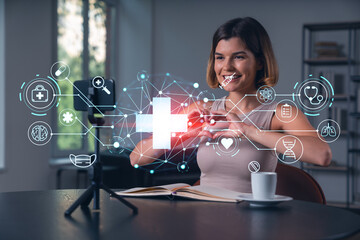 Happy woman is making video blog using smartphone on a tripod explaining with hands at office workplace. Concept of online stream, business education, conference call. Medical health care hologram