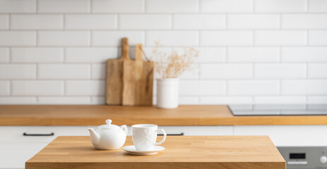 Wooden oak table with a cup of tea and a kettle in front of the kitchen with a white brick background - Powered by Adobe