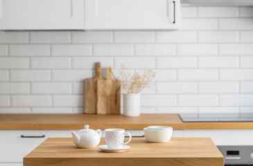 Fototapeta na wymiar Wooden oak table with a cup of tea and a kettle in front of the kitchen with a white brick background