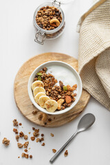 Granola with banana and nuts on a wooden board on a white table with a napkin and spoon.