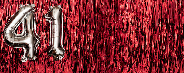 Silver foil balloon number 41 on a background of red tinsel decoration. Birthday greeting card,...