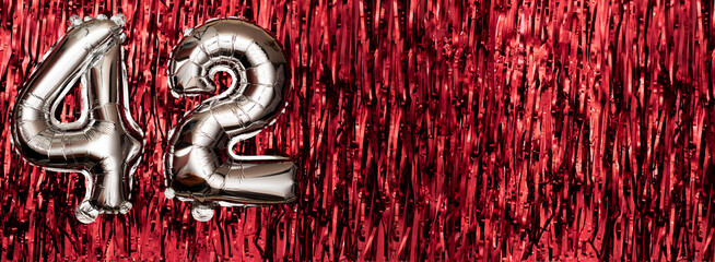 Silver foil balloon number 42 on a background of red tinsel decoration. Birthday greeting card,...