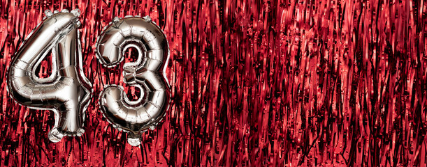 Silver foil balloon number 43 on a background of red tinsel decoration. Birthday greeting card,...