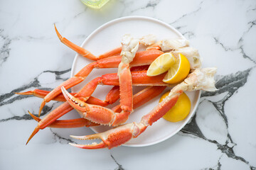 Boiled crab legs and claws with lemon wedges on a white marble background, horizontal shot, flat lay