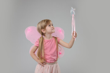 Cute little girl in fairy costume with pink wings and magic wand on light grey background