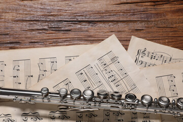 Sheets with musical notes and flute on wooden table, flat lay