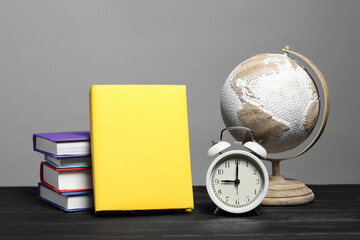 Different books, globe and alarm clock on black wooden table against gray background