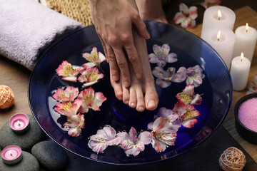 Obraz na płótnie Canvas Woman putting her foot in bowl with water and flowers on floor, closeup. Spa treatment