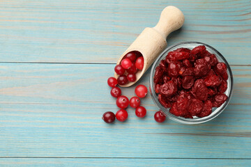 Tasty dried cranberries in bowl and fresh ones on light blue wooden table, top view. Space for text