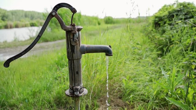 A water pouring out of deep well faucet standing near a lake in grass