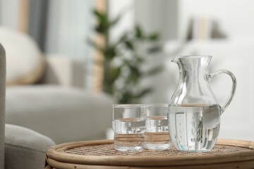 Jug and glass with water on wicker table against blurred background. Space for text