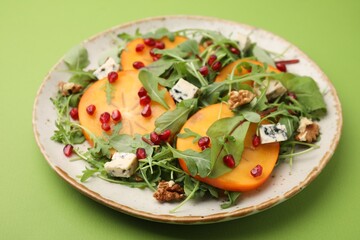 Tasty salad with persimmon, blue cheese and walnuts served on light green background
