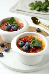 Delicious creme brulee with berries and mint in bowls on white table, closeup