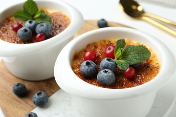 Delicious creme brulee with berries and mint in bowls on table, closeup