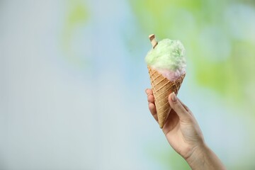 Woman holding waffle cone with cotton candy on blurred background, closeup. Space for text
