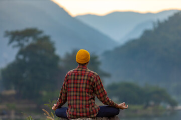 Rear view of man is relaxingly practicing meditation yoga in forest in summer to attain happiness from inner peace wisdom with morning light for healthy mind and soul concept