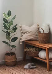 Foto op Canvas A cozy corner of the living room - a wooden bench with a pillow and a blanket, baskets, a ficus flower, slippers on a jute carpet. A cozy house © okkijan2010